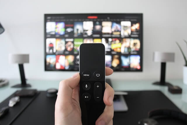 a remote control being held in a hand with a television screen in the background