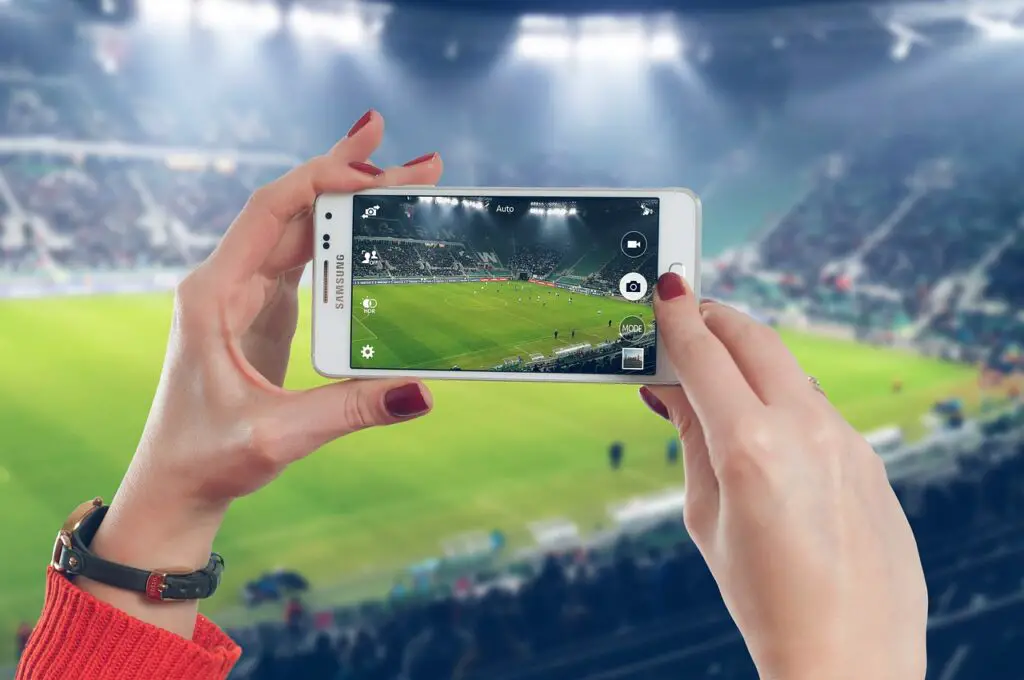 woman filming or taking a photo of a live sports game at a stadium with a smartphone