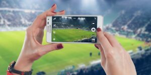 woman filming or taking a photo of a live sports game at a stadium with a smartphone