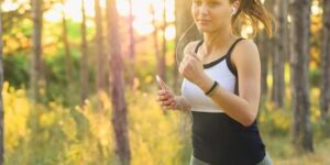 woman jogging through a forest while listening to music on a smartphone