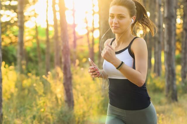 woman jogging through a forest while listening to music on a smartphone